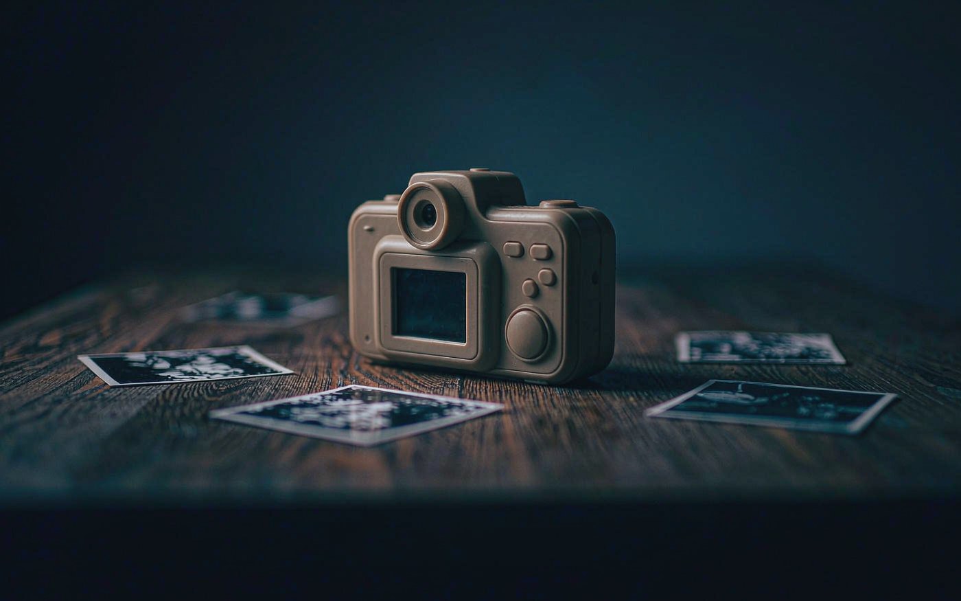 A chunky plastic kids camera on a dark wooden table with small printed photos scattered around it