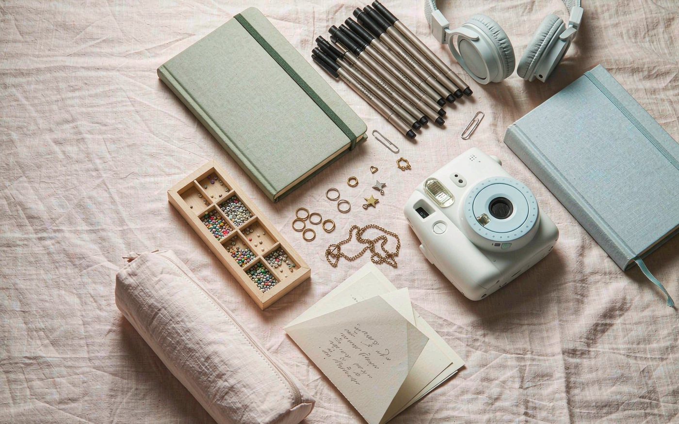Flat lay of gifts for a 10 year old girl: sketchbook, fine liner pens, jewellery making beads and brass findings, instant camera, cloth bound book and headphones