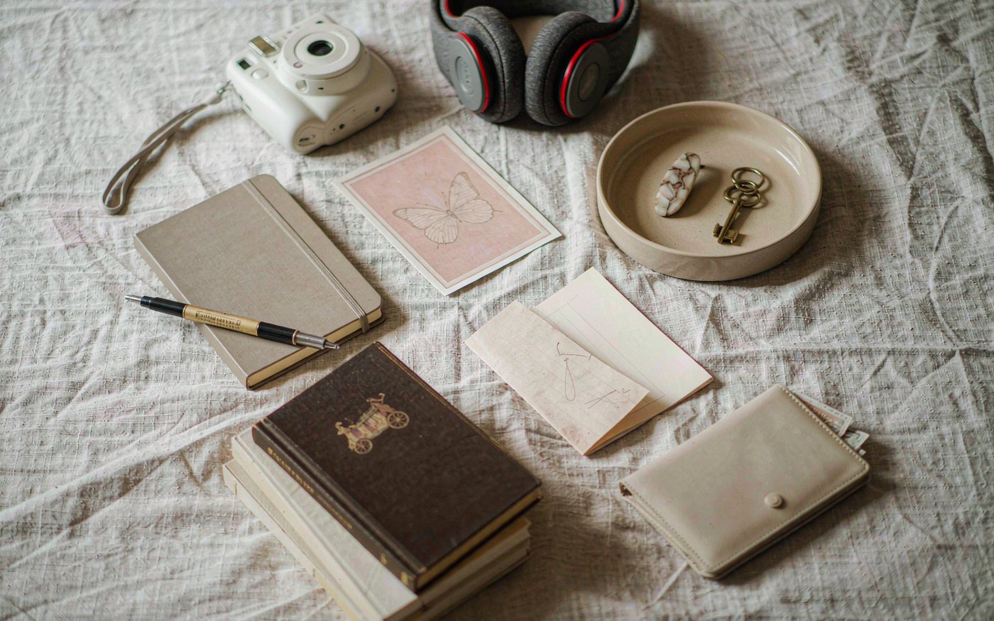 Flat lay of gifts for a 12 year old girl: instant camera, headphones, hardbound sketchbook and pen, cloth bound books, ceramic dish and a small wallet
