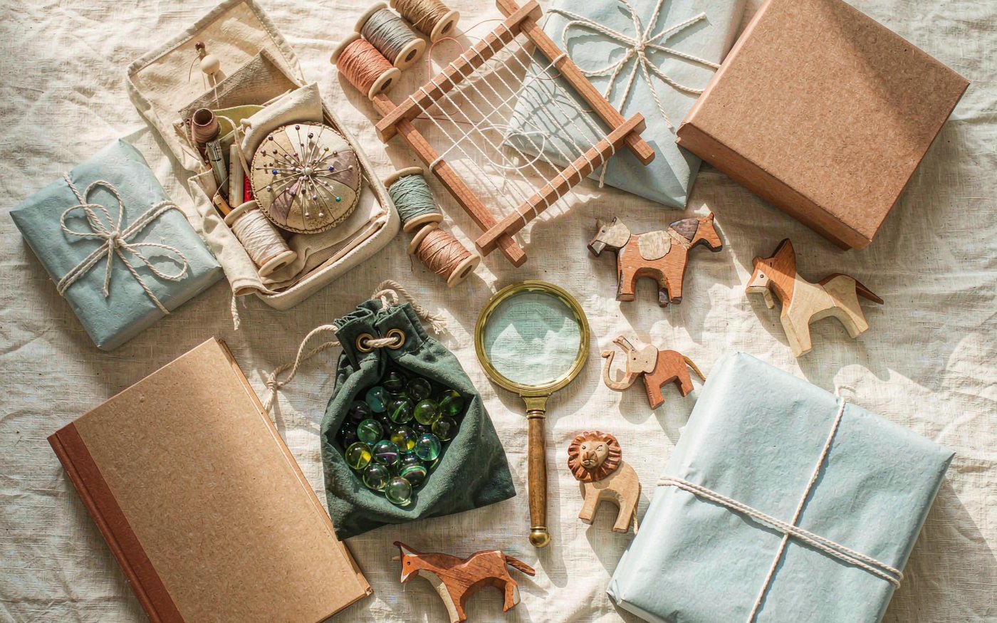 Flat lay of gifts for an 8 year old girl: sewing kit, bead loom, hardback book, marbles in a cloth bag, magnifying glass and wooden animal figures