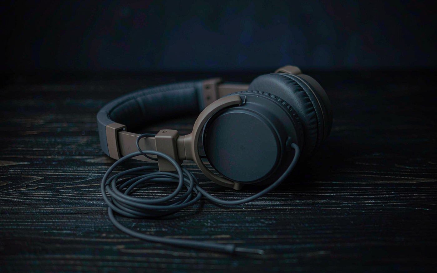 A pair of small over-ear headphones with a coiled cable lying on a dark wooden table