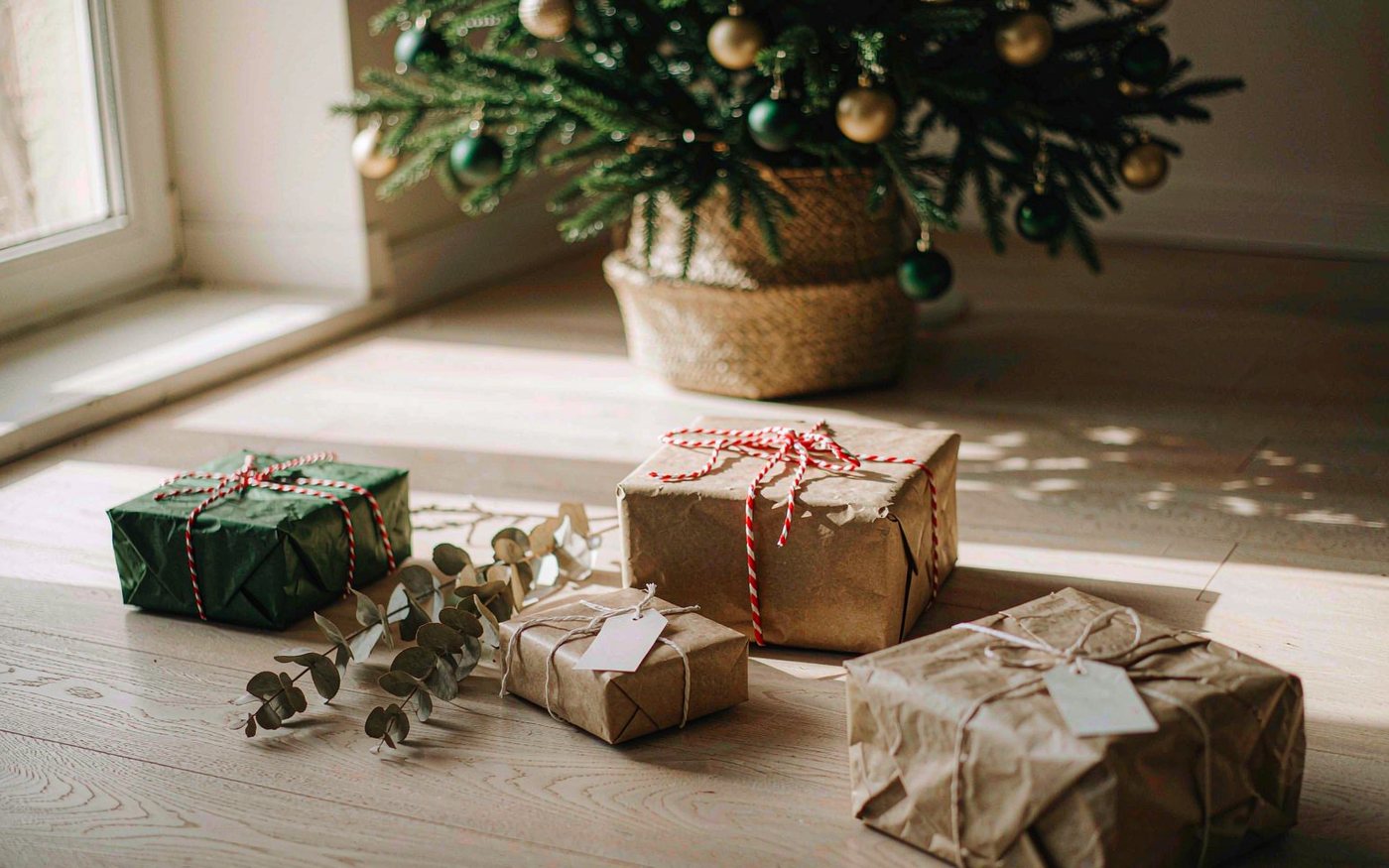 Wrapped children Christmas gifts in kraft paper and dark green paper with red twine on a wooden floor beside a Christmas tree